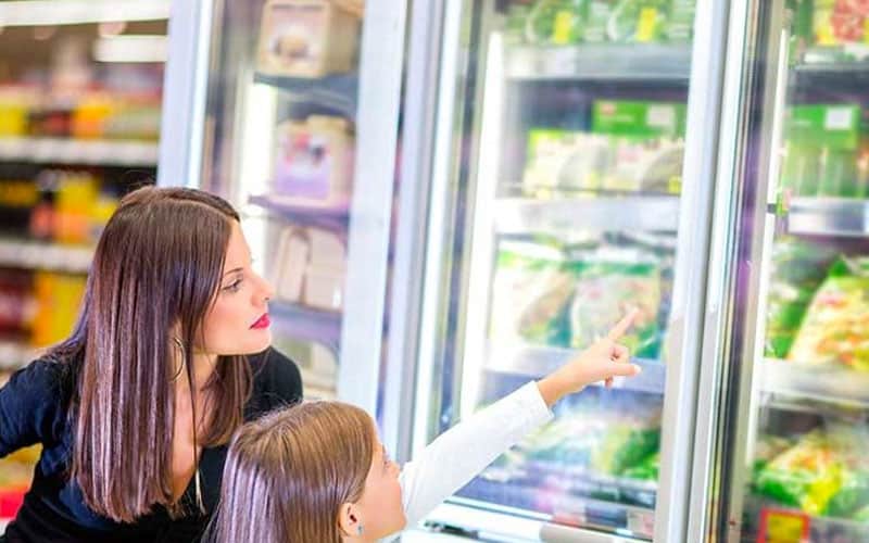 A little girl pointing to food in the freezer case, at the grocery store with her mom